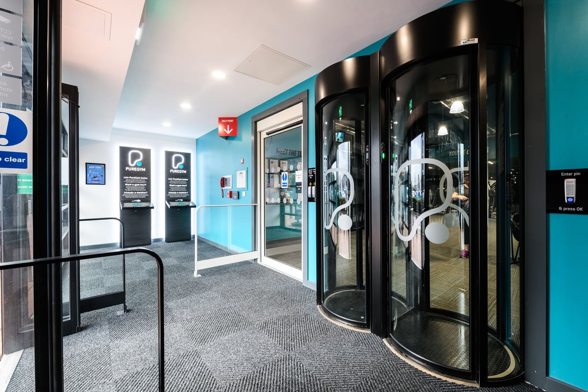PureGym Cardiff Bay: Glass revolving doors, rubber floor mats, turquoise walls, parking signs.