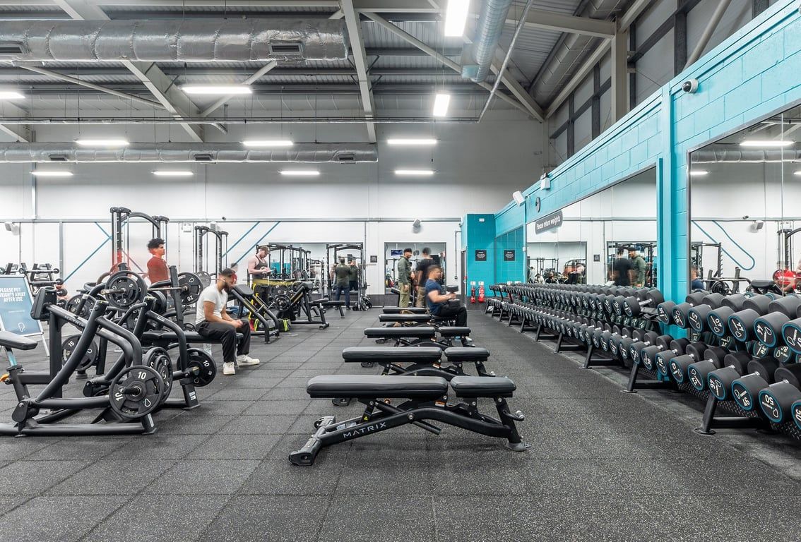 PureGym Birmingham West: Large gym studio with rows of weight machines, free weights, benches, and rubberized flooring.
