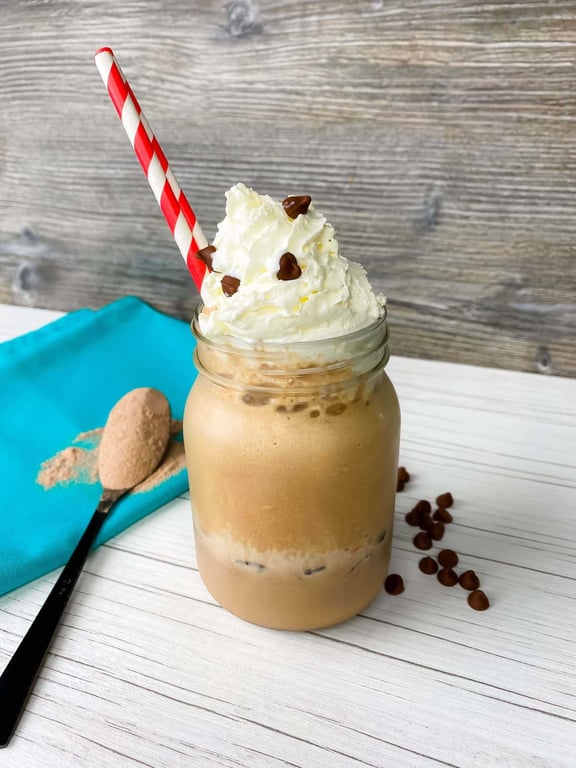 Iced coffee with whipped cream and chocolate chips in a jar with a red striped straw