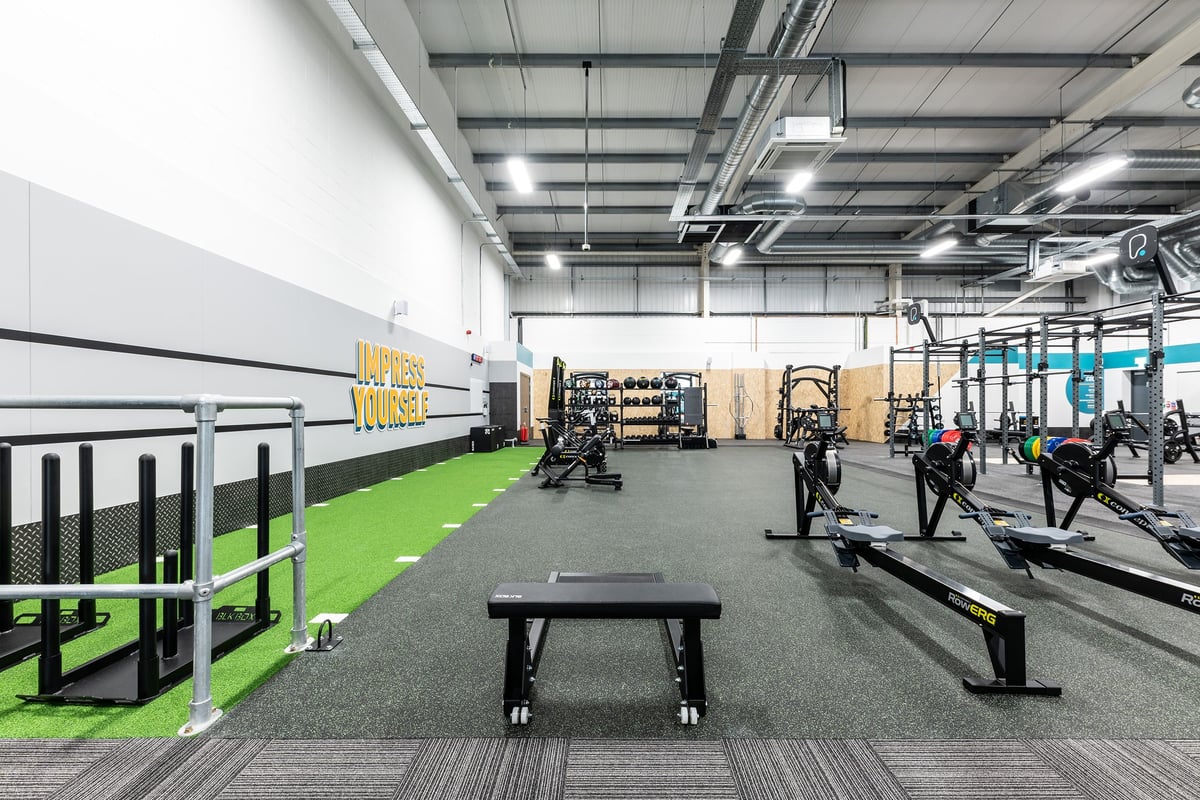 PureGym Great Yarmouth: Weightlifting area with squat racks, benches, turf section, and rubberized floors.