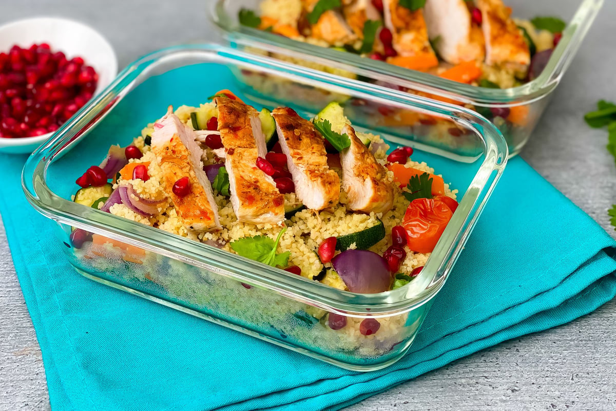 Sliced grilled chicken on couscous with vegetables and pomegranate in glass container