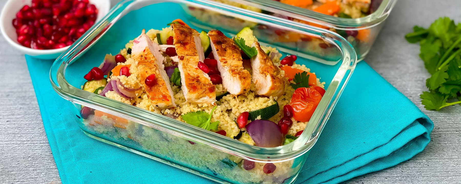 Sliced grilled chicken on couscous with vegetables and pomegranate in glass container