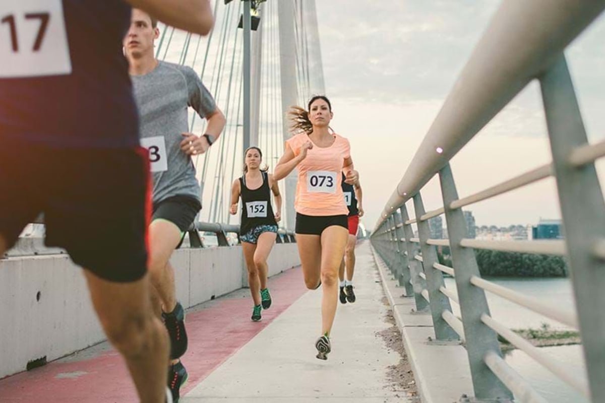 Runners with numbered bibs competing on a bridge pathway during a race.