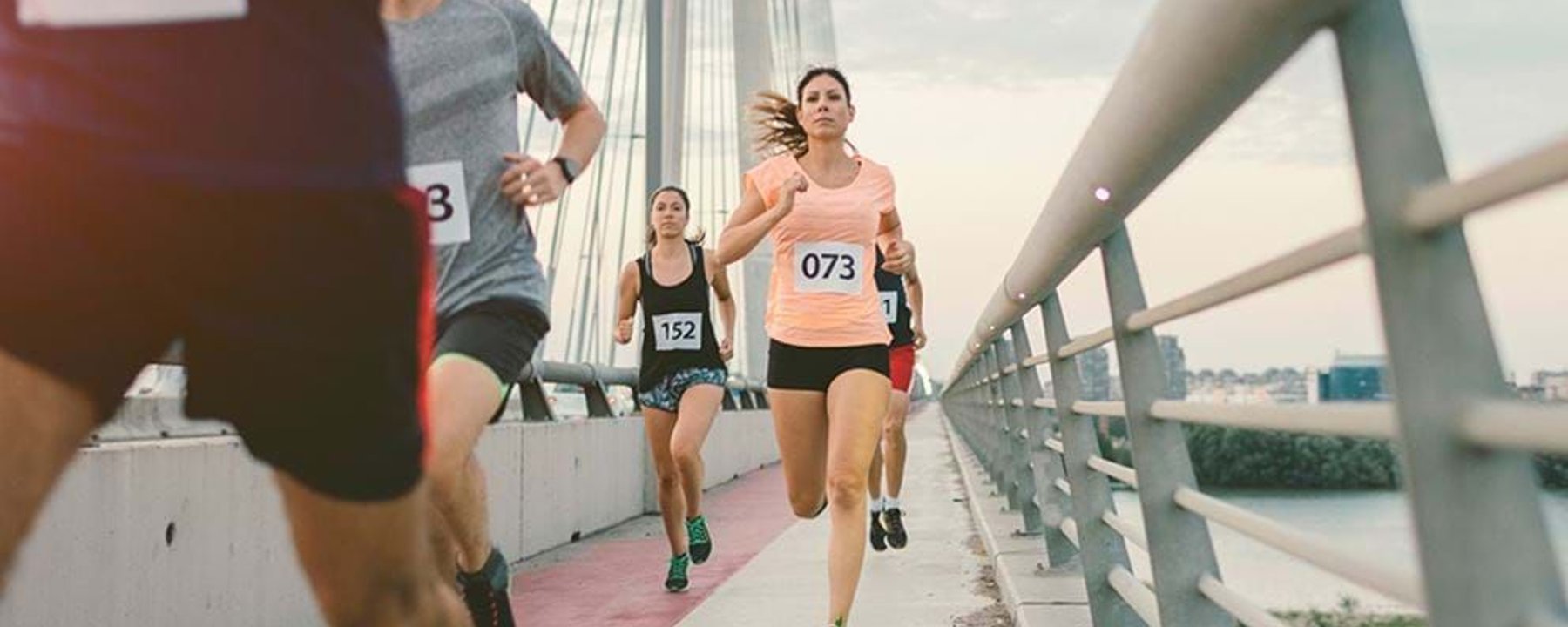 Runners with numbered bibs competing on a bridge pathway during a race.