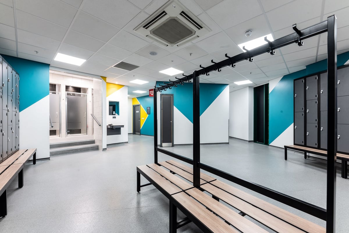 PureGym Newcastle Eldon Garden: Rows of weight racks, benches, mirrors, and colourful wall decor in a gym changing area.