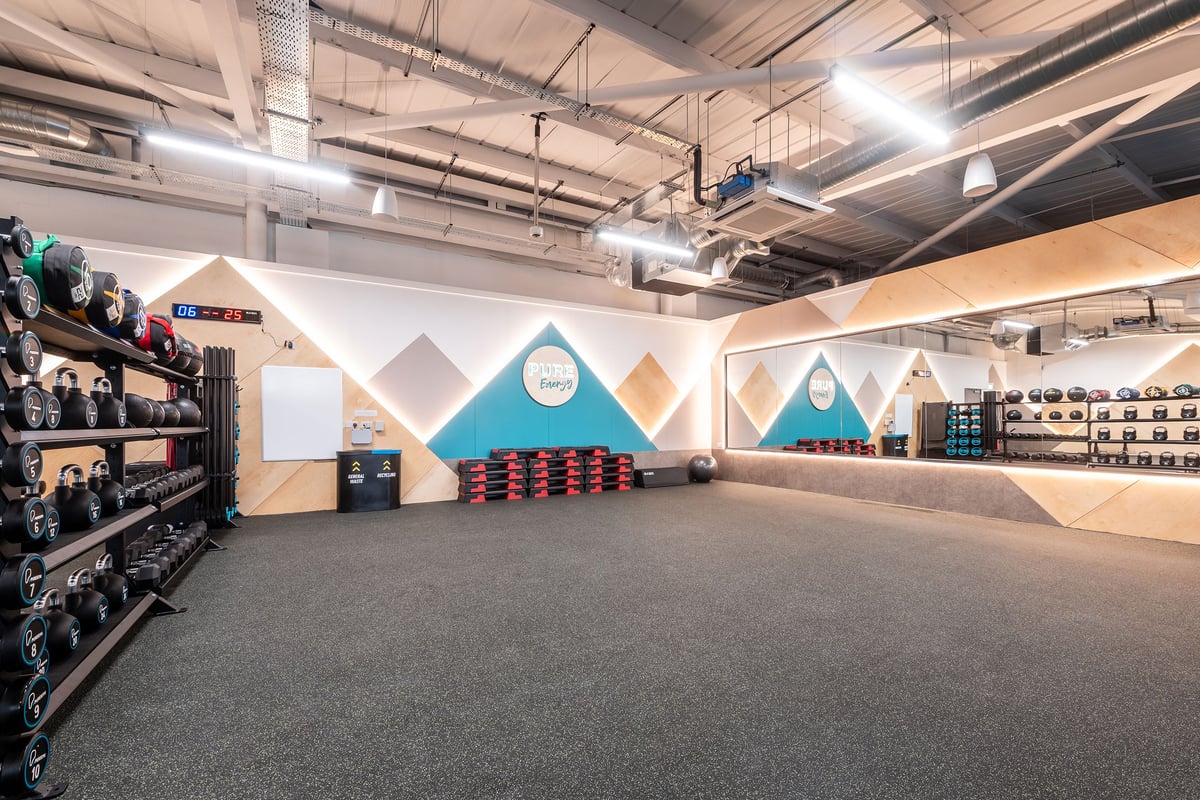 PureGym Bideford: Free weight racks, rubberized flooring, geometric wall art, mirrored walls in fitness studio.