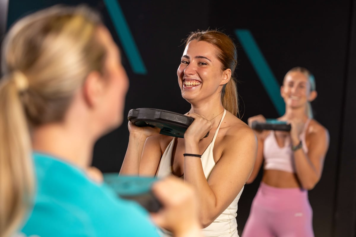 Three women lifting weights in a gym with black walls and blue stripes
