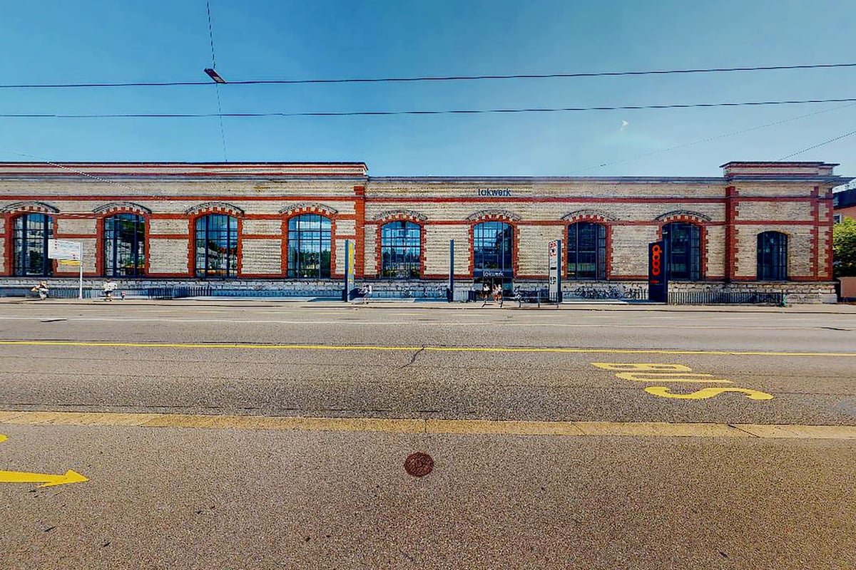 PureGym Winterthur Töss: Extérieur du bâtiment avec de grandes fenêtres et des marques routières sur la chaussée au premier plan.