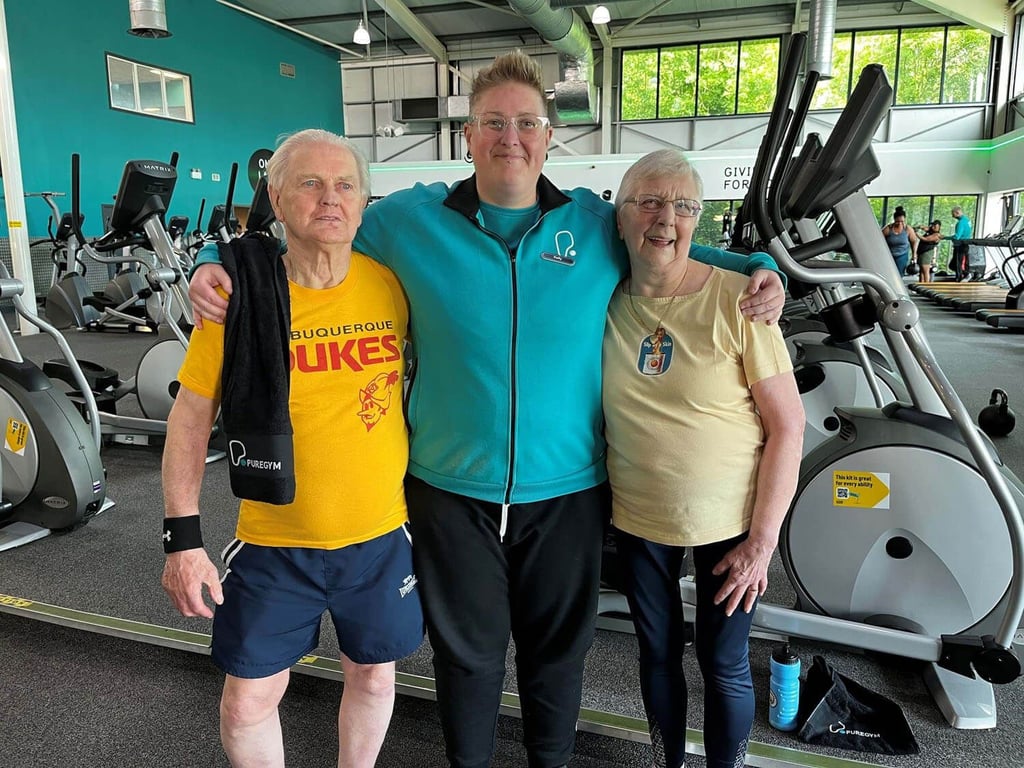 Three people standing with arms around each other in a gym with exercise machines