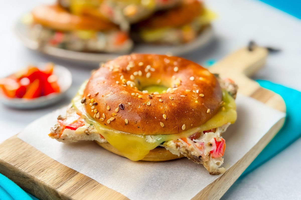 Sesame bagel sandwich with melted cheese and chicken on a wooden board