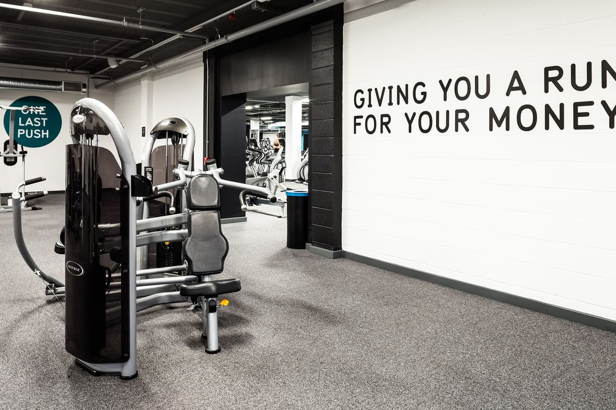 PureGym Altrincham: Weight machines, benches, rubberized flooring, and a sign stating "Giving you a run for your money."