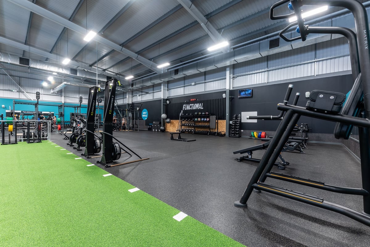 PureGym Widnes: Functional training area with green turf, squat racks, weightlifting platforms, and rubberized flooring.