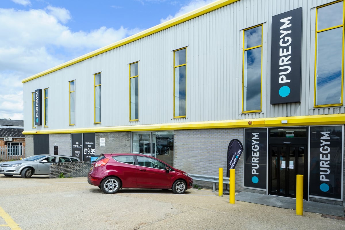 PureGym Billericay: Gym storefront with yellow trim, parking spaces, and sign displaying "Puregym" branding.