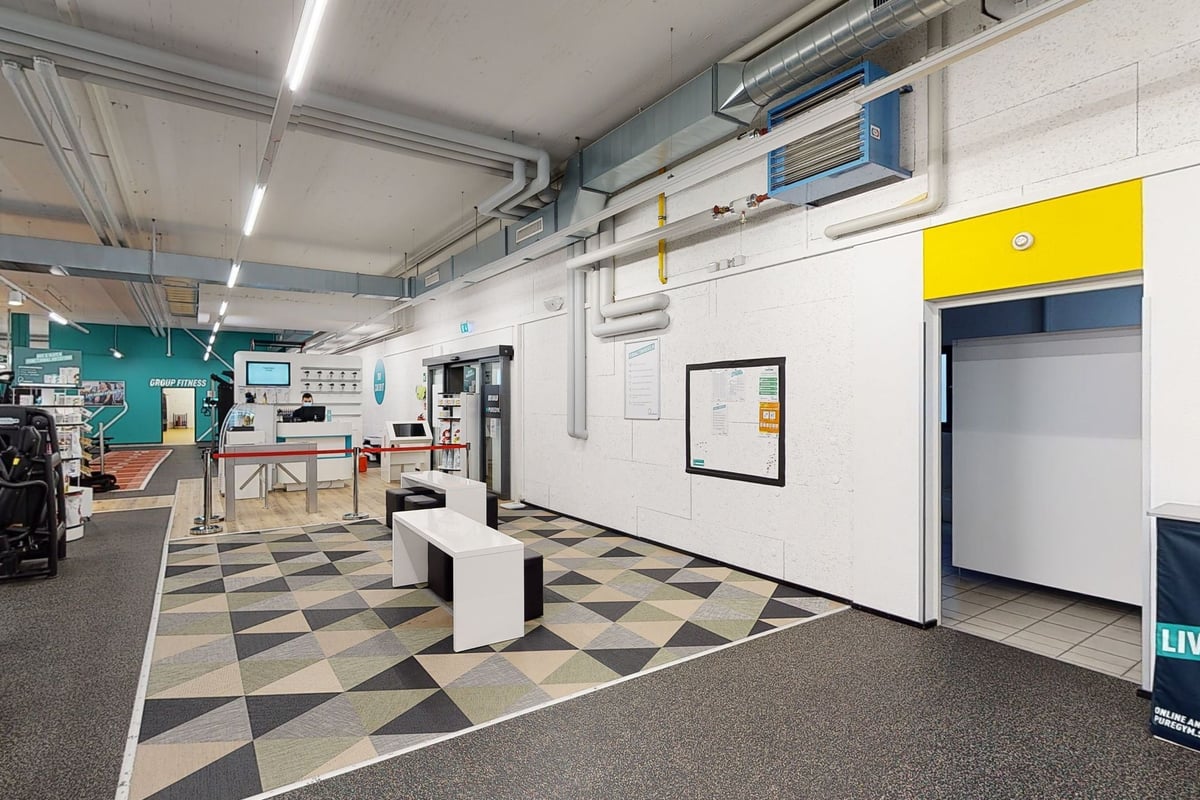 PureGym Pfäffikon: Innenraum des Fitnessraums mit Trainingsgeräten, Fliesenboden, HLK-Kanälen, Bänken und Spiegeln an den Wänden.