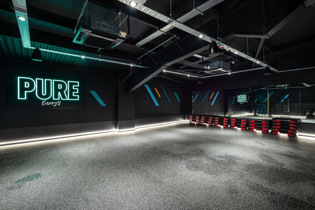PureGym Stratford-upon-avon: Rows of red benches, neon 'PURE' signage, and industrial ceiling in dimly lit space.