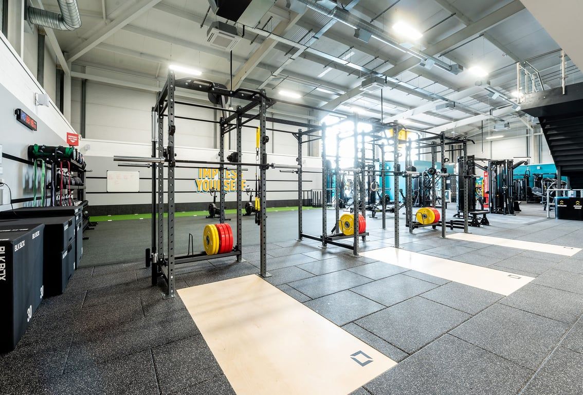 PureGym Trowbridge: Weightlifting racks, colourful bumper plates, squat racks, rubberised flooring in a gym facility.
