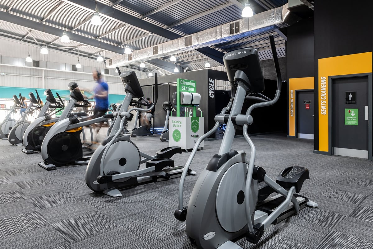 PureGym Warrington Central: Rows of stationary bikes, ellipticals, treadmills, with kiosks along the walls.
