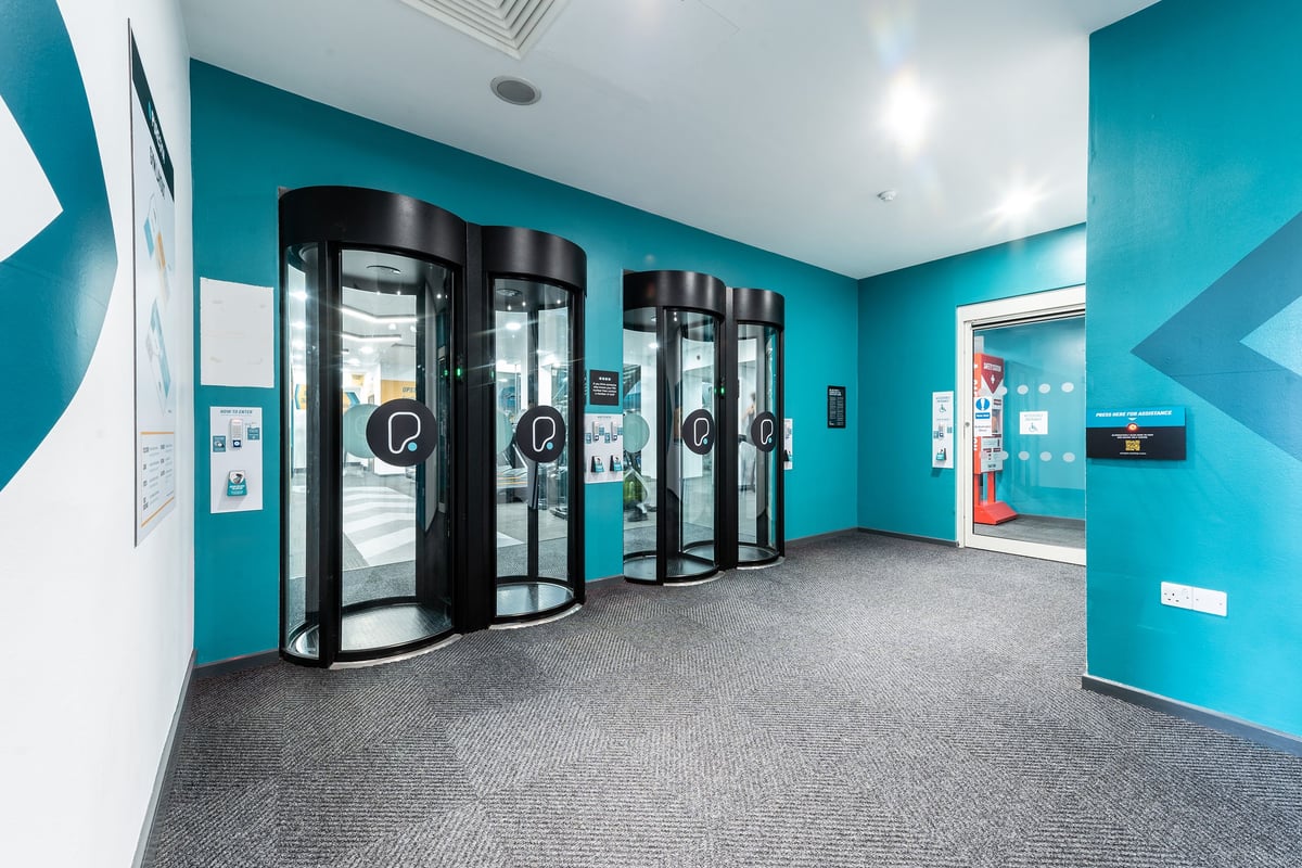 PureGym London Bayswater: Entrance pods, teal walls, and grey carpeted floor in the entrance area.