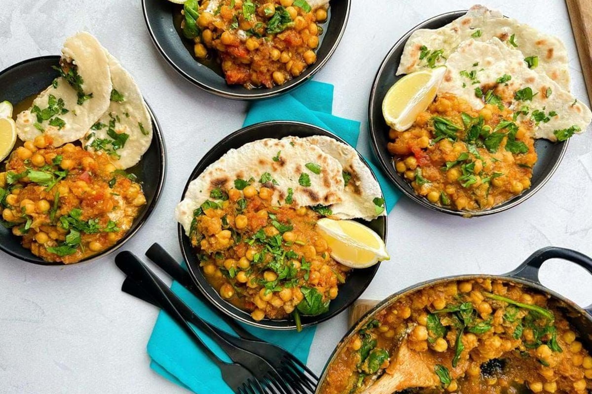 Bowls of chickpea curry with flatbread and lemon wedges on a white surface