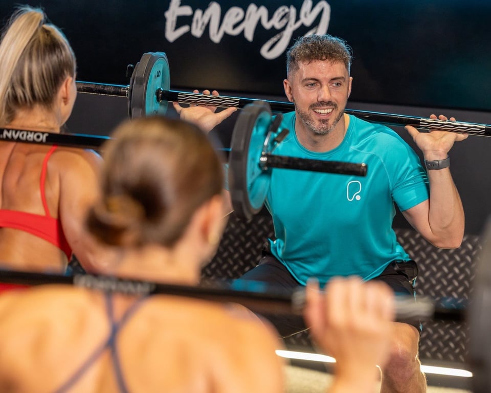 Male instructor in turquoise shirt leading group fitness class with weighted bars