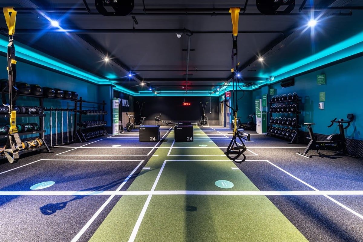 PureGym London Bank: Squat racks, benches, free weights, rubberized flooring in a dimly lit studio with blue accent lighting.