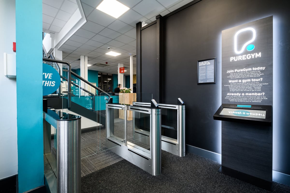 PureGym London Bow Wharf: Turnstiles, advertising signage for Pure Gym, and a reception area interior.