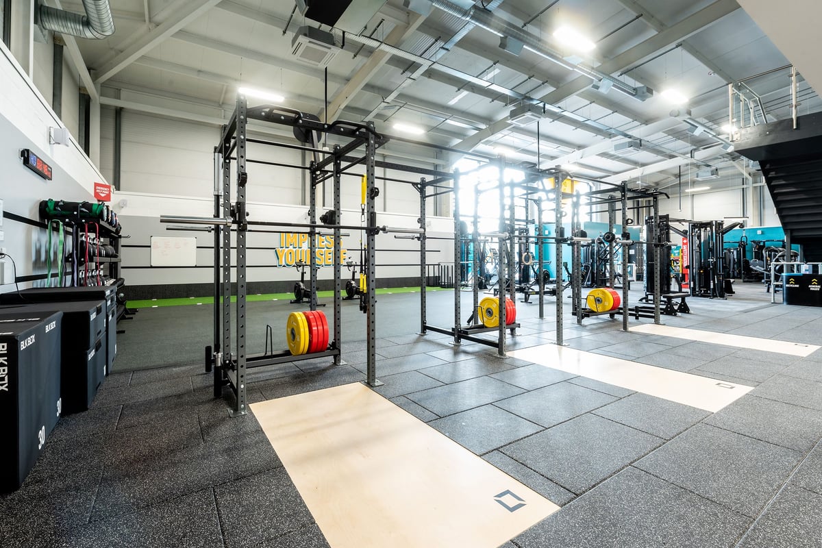 PureGym Trowbridge: Weightlifting racks, colourful bumper plates, squat racks, rubberised flooring in a gym facility.