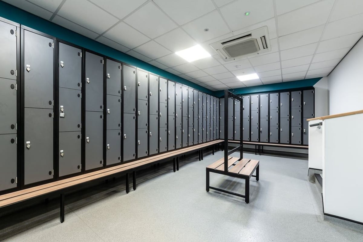 PureGym Ipswich Buttermarket: Rows of lockers, wooden benches in a teal room interior.
