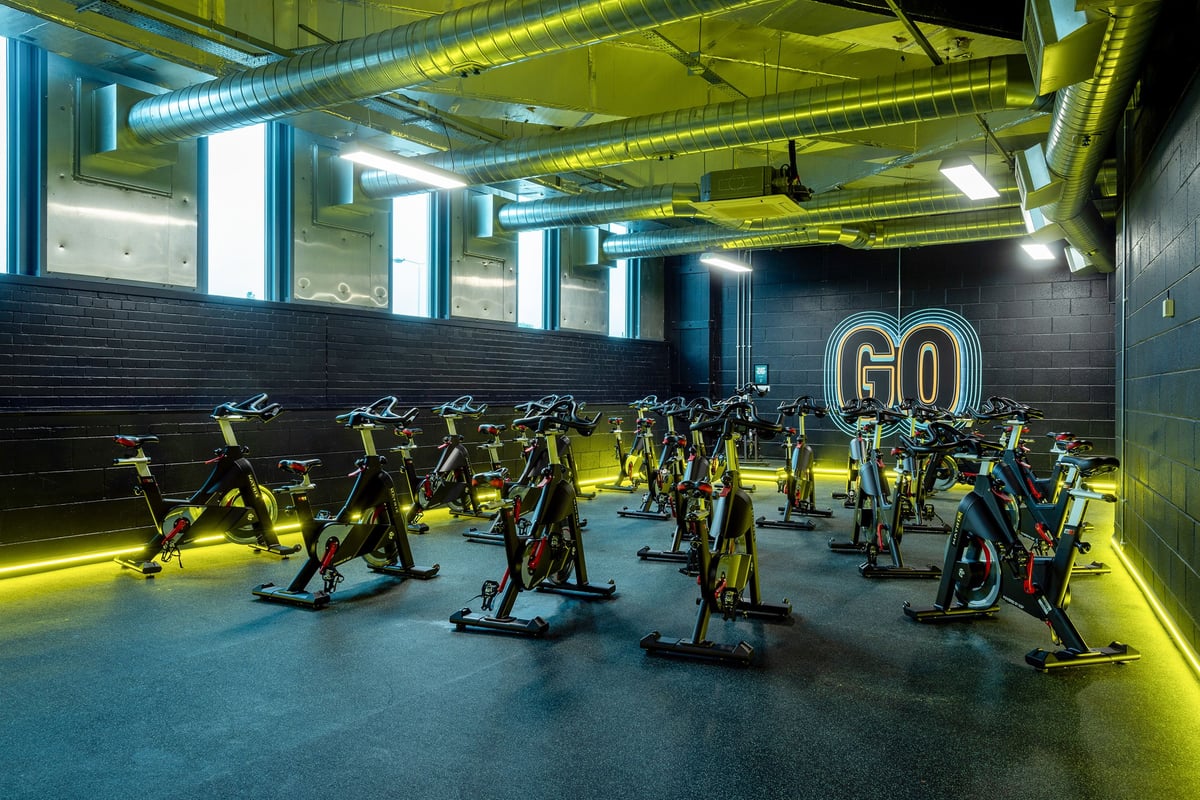 PureGym Leicester St Georges Way: Rows of spin bikes inside a dimly lit studio with exposed ducts and neon "GO" signage.