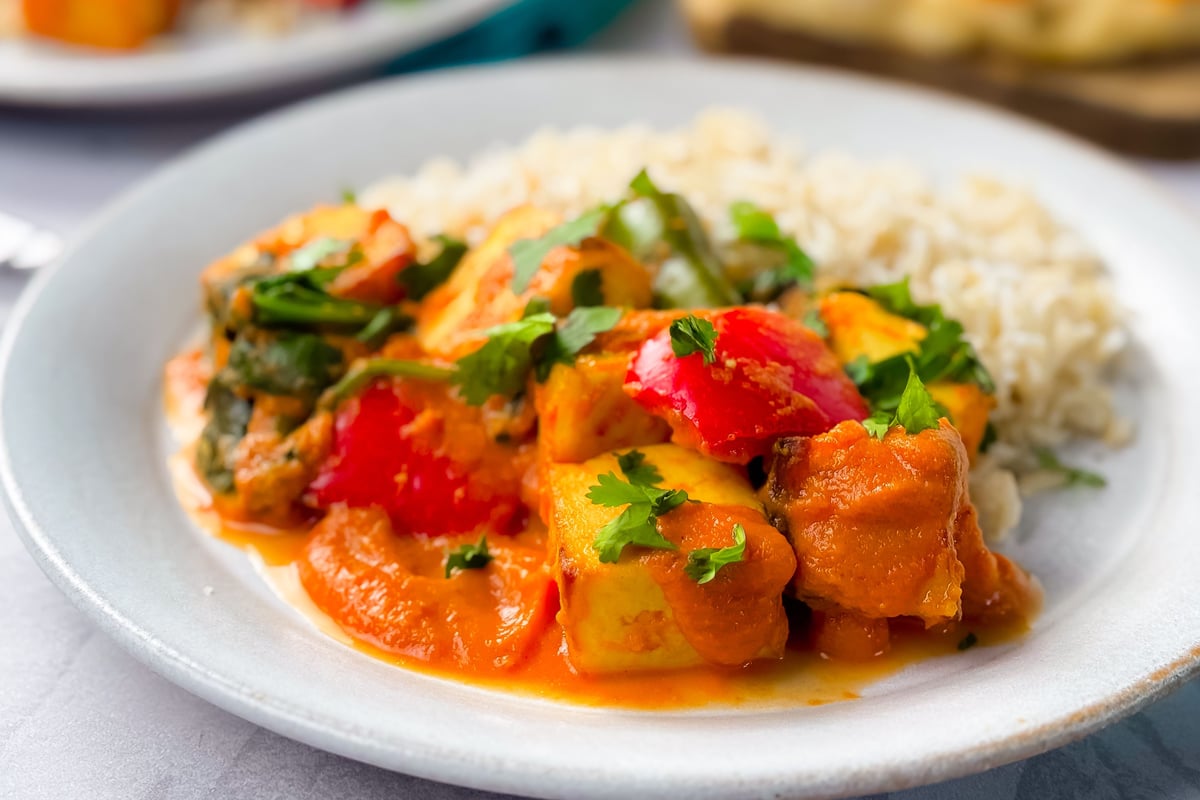Paneer tikka masala with peppers and coriander served with rice on a white plate