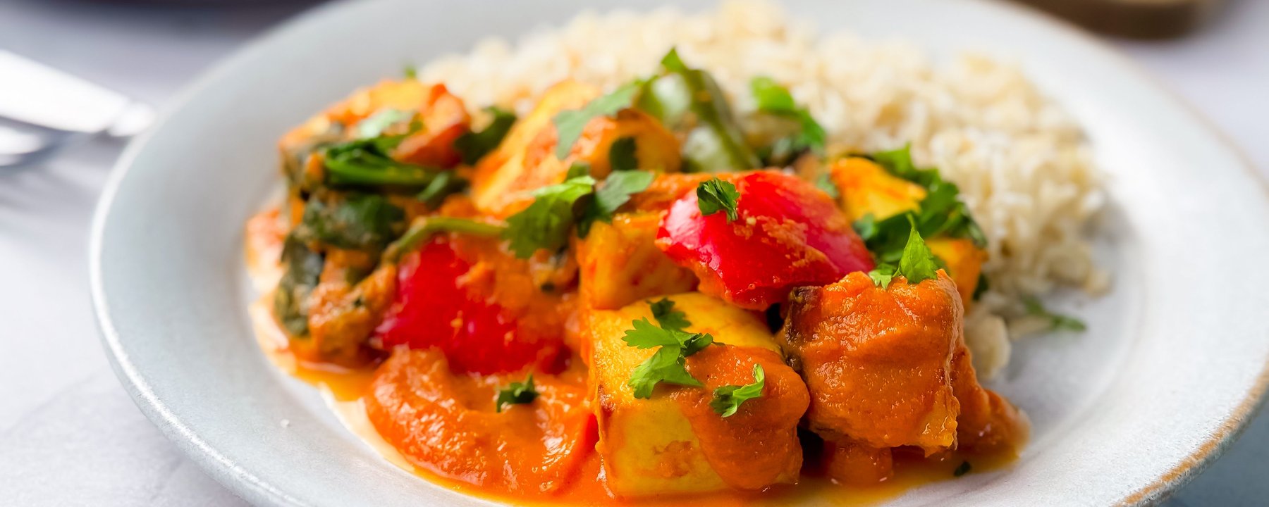 Paneer tikka masala with peppers and coriander served with rice on a white plate