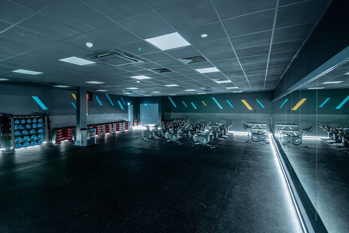 PureGym Belfast Boucher Road: Rows of stationary bikes, treadmills, and weight training machines in a dimly lit gym interior.