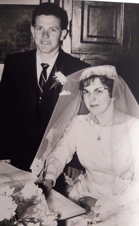 Bride in veil signing document with groom standing beside her in suit and tie