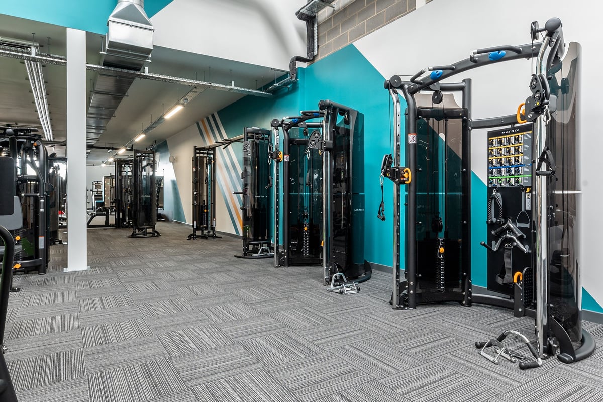 PureGym Sittingbourne: Rows of resistance machines, cable pulleys, and rubberized flooring in a teal-themed gym interior.