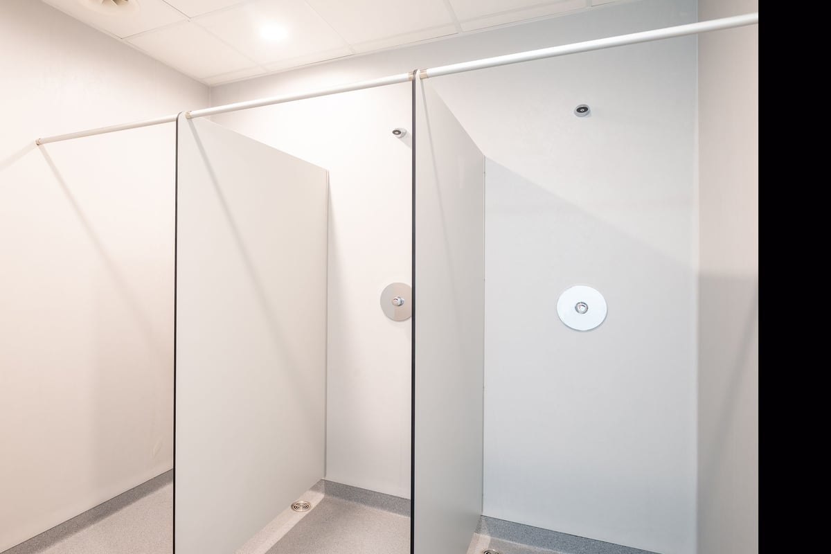PureGym Genf Le Bouchet: Shower area with floor-to-ceiling glass panels, tile flooring, rainfall showerheads.