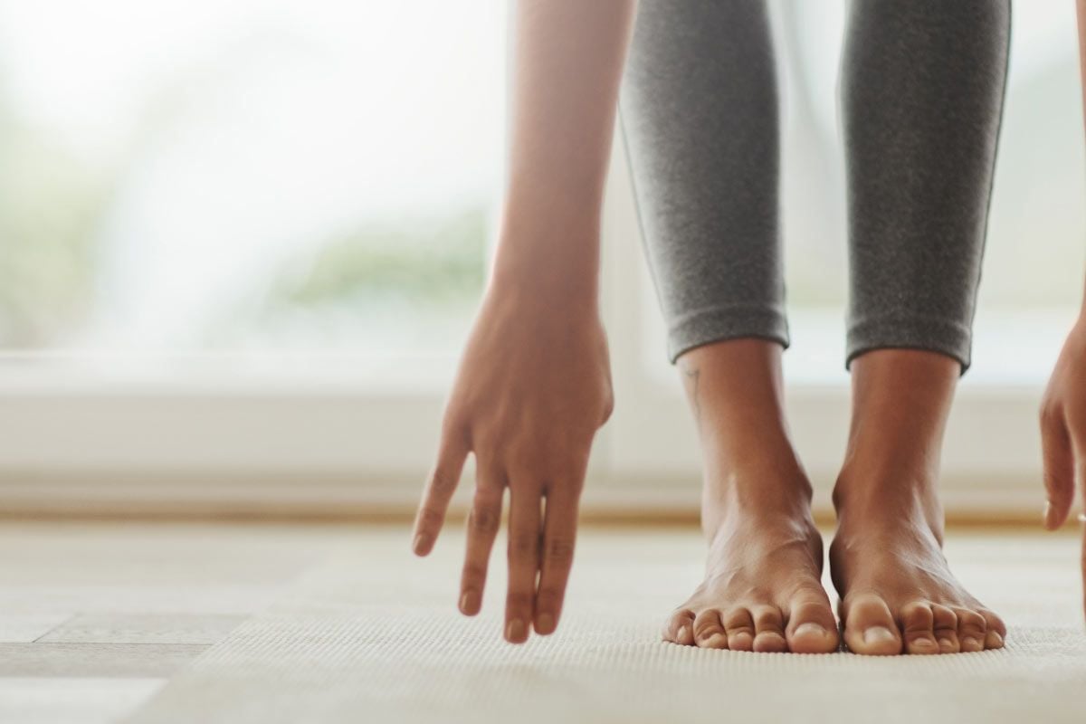 Drei Personen in Yogaposition mit Händen und bloßen Füßen auf einer Matte neben einem Fens