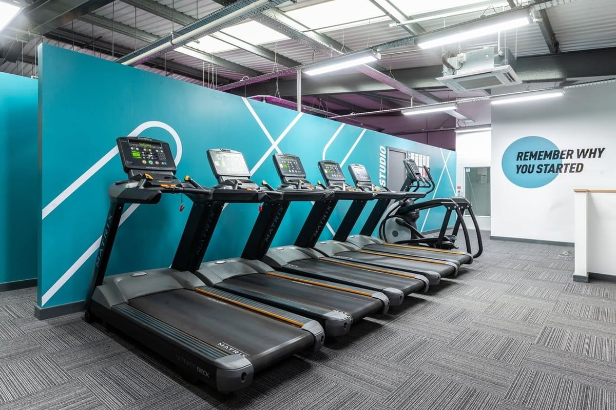 PureGym Oldham: Row of modern treadmills against teal backdrop in fitness studio.