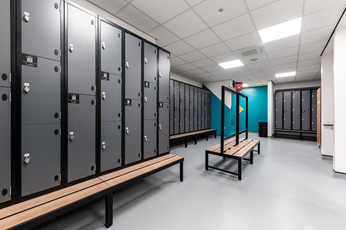 PureGym Doncaster: Rows of lockers, wooden benches, and tiled flooring in a changing room area.