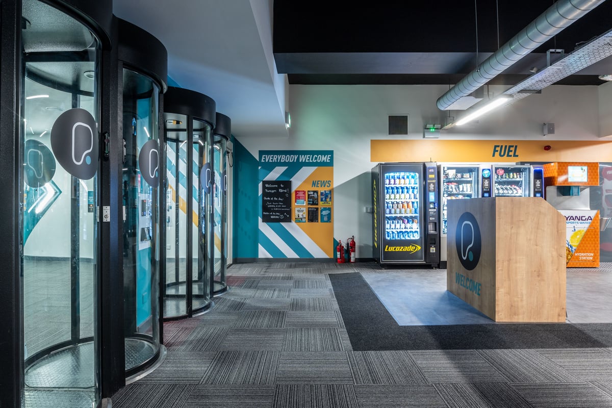PureGym London Ilford: Vending machines, turnstiles, floor tiles, bench, commercial gym lobby.