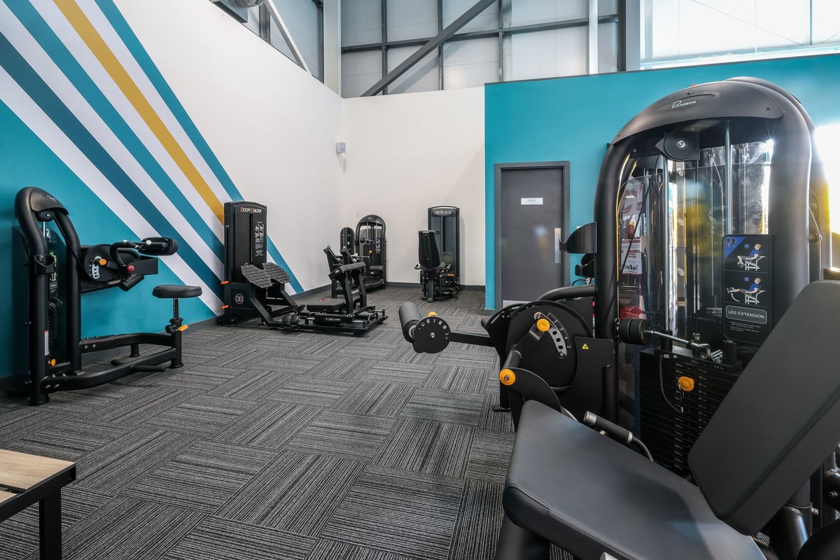 PureGym Bishop Auckland: Resistance machines, a VR rig, rubberized flooring, and striped accent wall inside a gym studio.