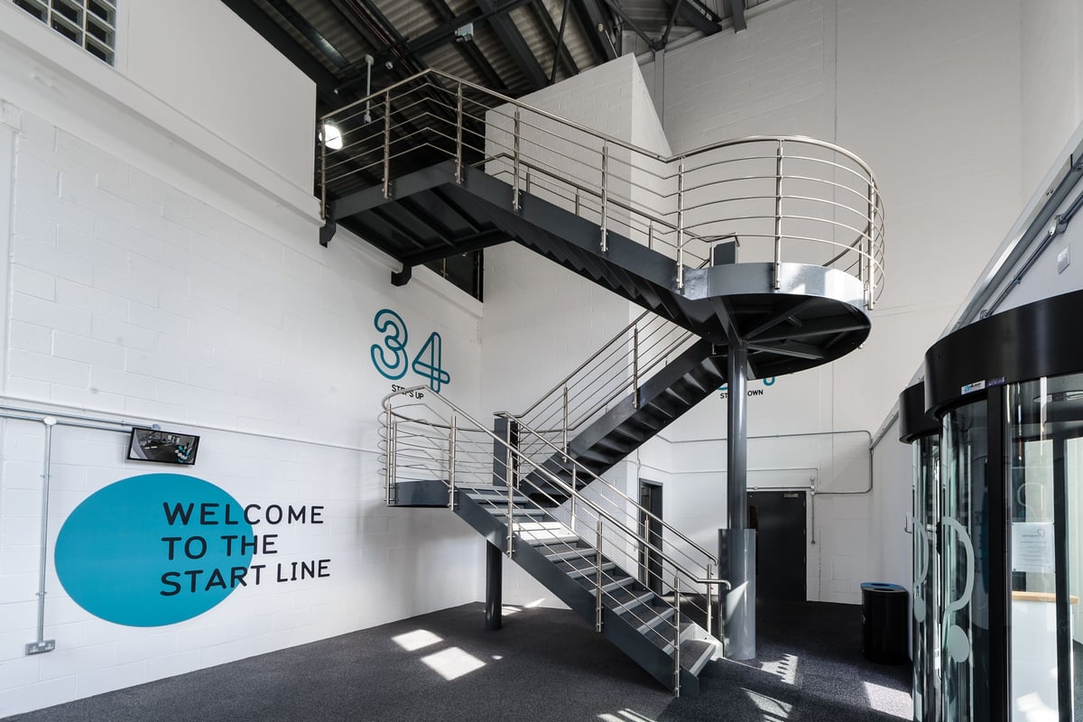 PureGym Worcester: Spiral staircase, metal railings, and wall signage reading "WELCOME TO THE START LINE".