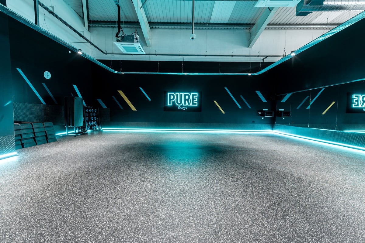 PureGym Newbury: Indoor gym studio with neon blue lighting, mirrored walls, and rubberized flooring.