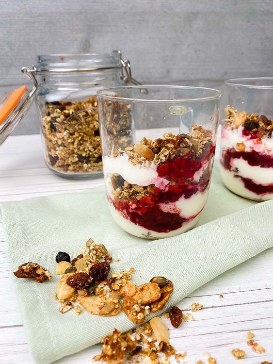Two glasses with layered yoghurt, berry compote, and granola on a cloth