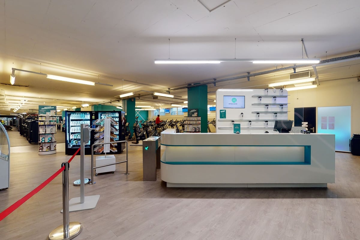 PureGym Basel Dreispitz: Gym welcome area with entrance turnstile, bending machines, information, and cycling bikes.