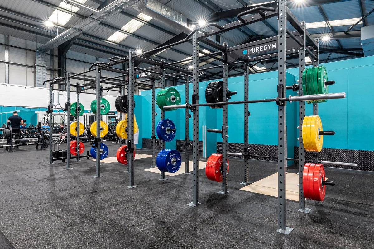 PureGym Leeds Hunslet: Squat racks, weight plates in various colours, rubberized flooring inside a weightlifting area.