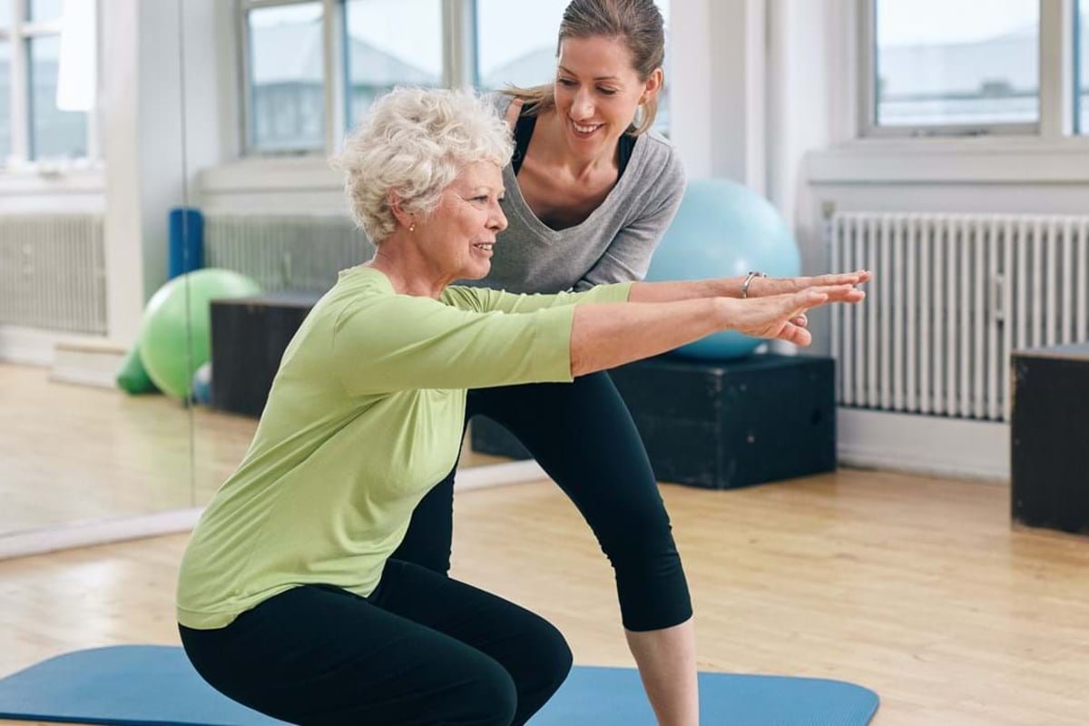 Older woman doing squats with trainer guiding her in gym studio
