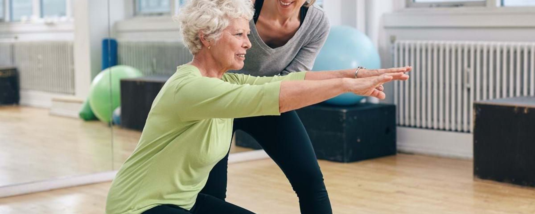 Older woman doing squats with trainer guiding her in gym studio