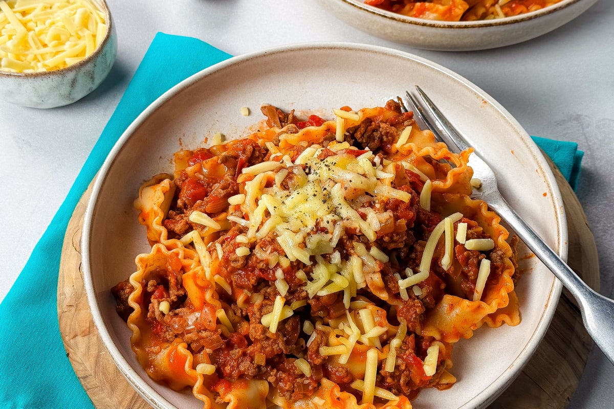 Bowl of pasta with beef mince and tomato sauce topped with grated cheese