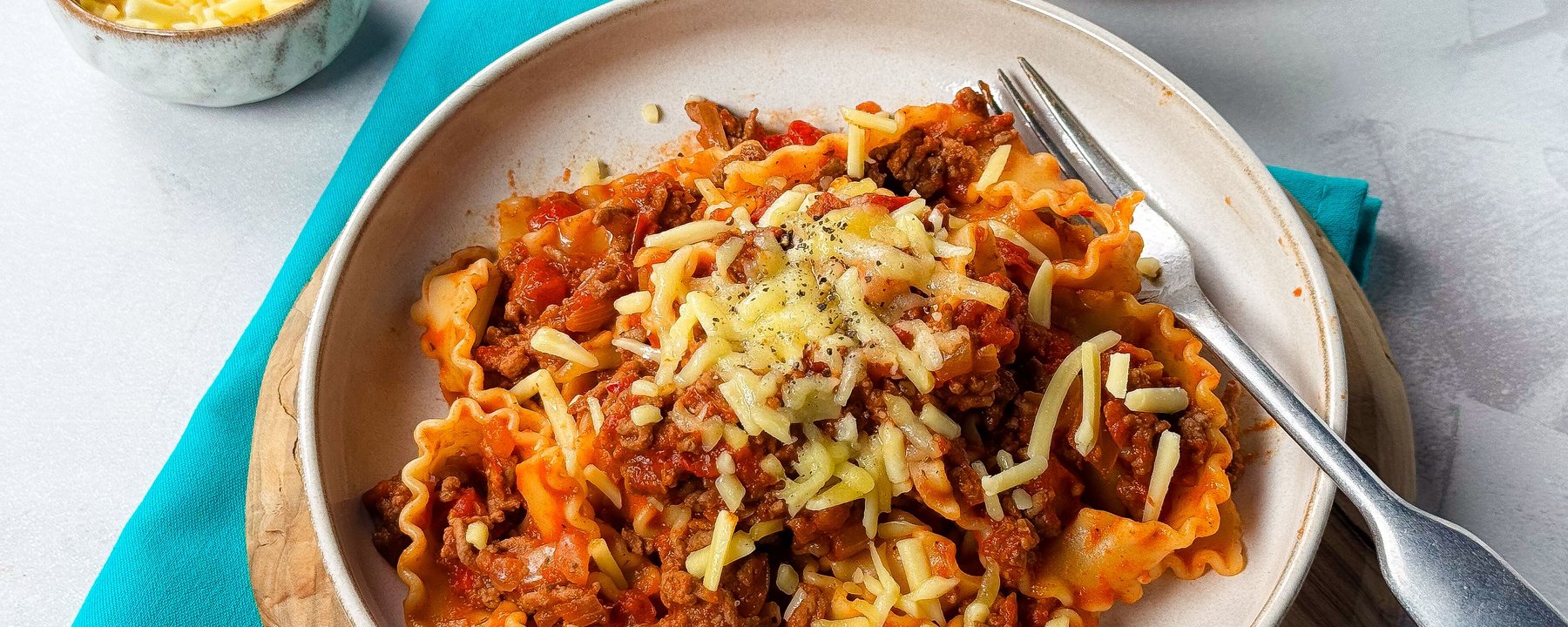 Bowl of pasta with beef mince and tomato sauce topped with grated cheese