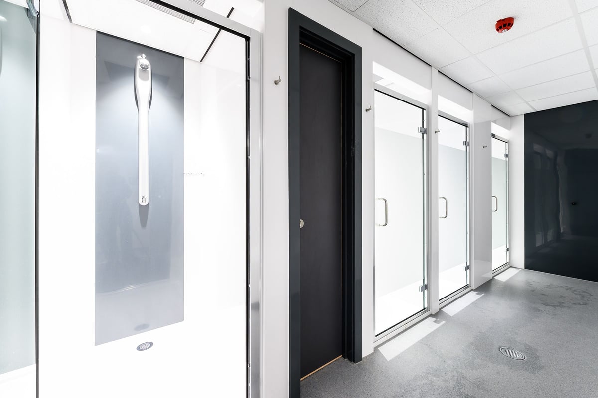 PureGym Bath Spring Wharf: Rows of glass-enclosed shower cubicles and changing rooms with lockers.